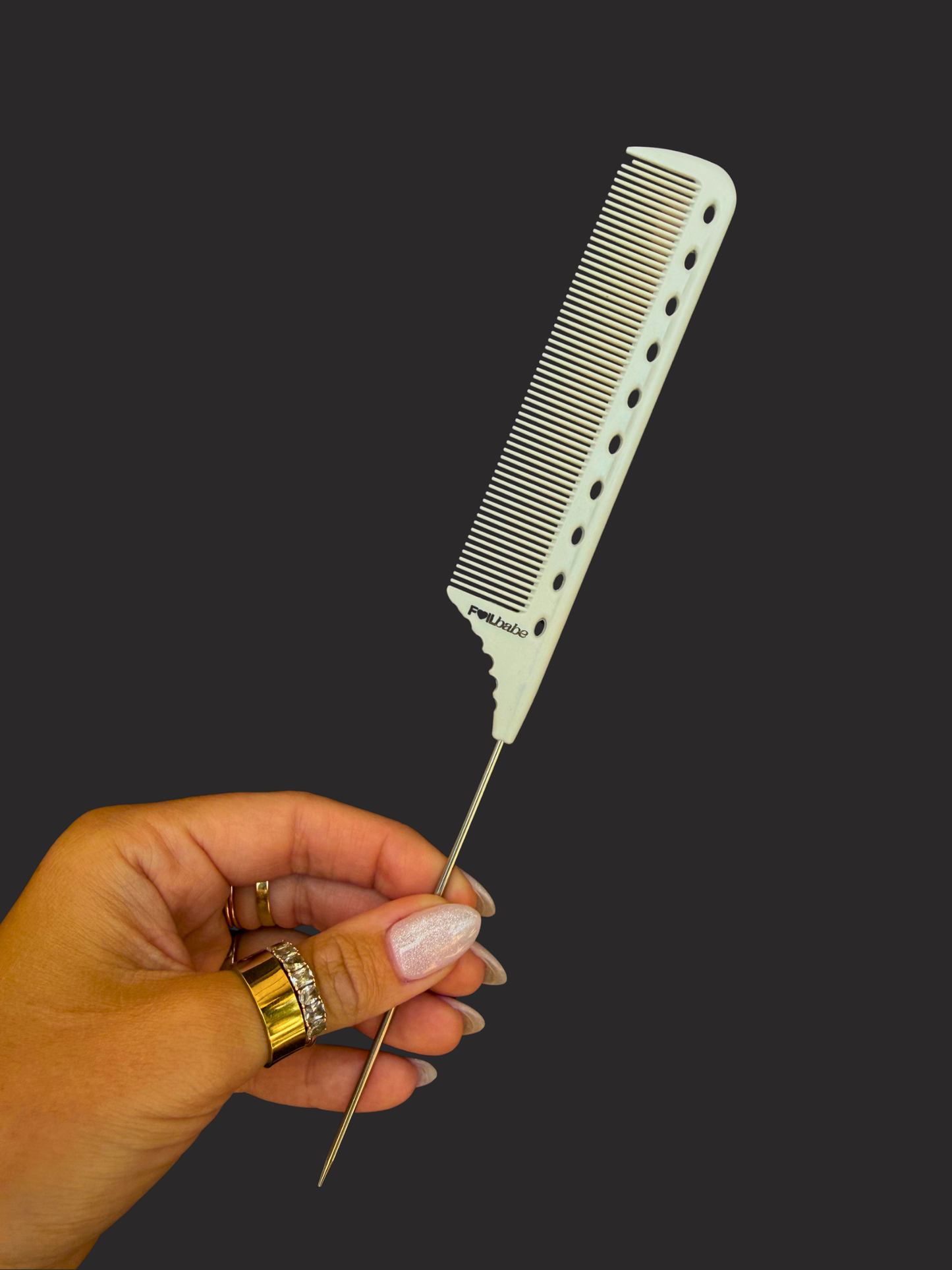 Hand holding a metal comb against a black background