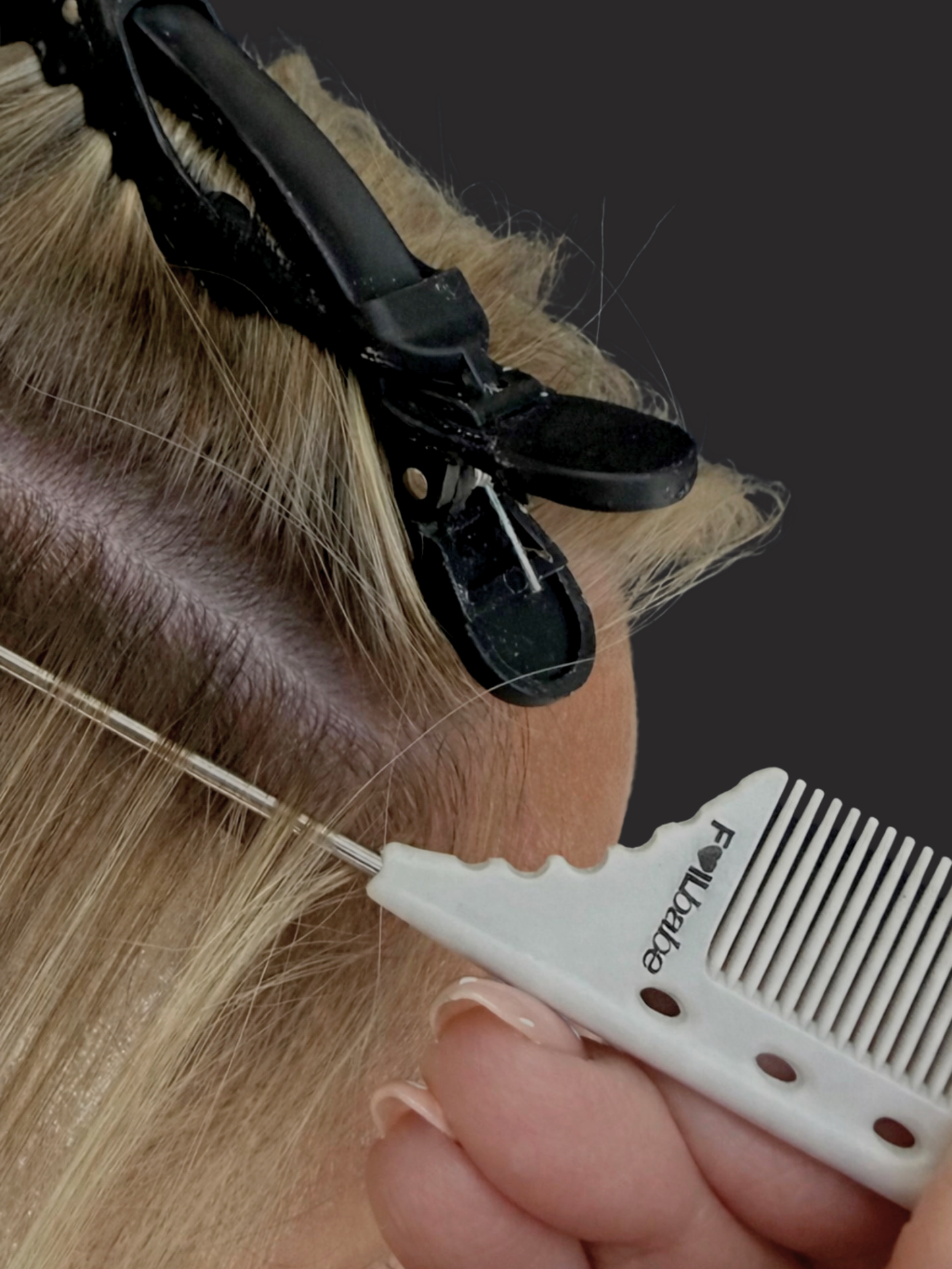Person applying hair extensions with a clip and comb on a dark background